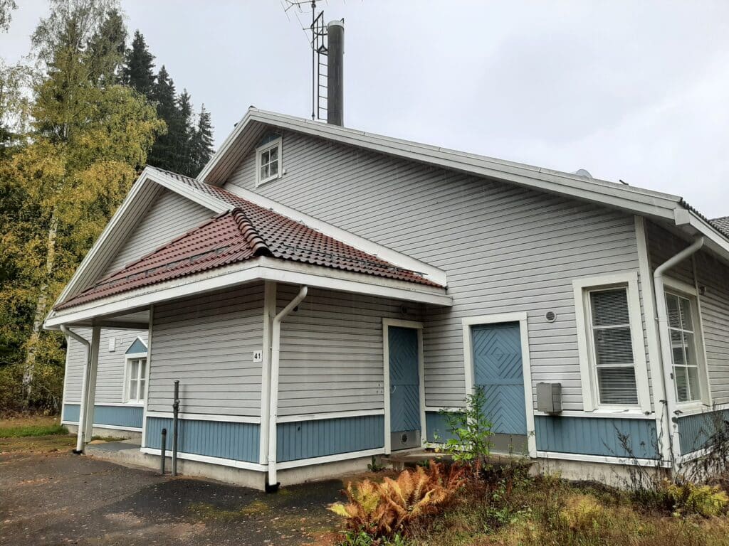 Kuva vaaleanharmaasta puisesta koulurakennuksesta.