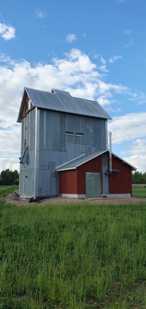 Viljankuivausrakennus maaseudulla, joka on verhoiltu maalaamattomalla aaltopellillä.